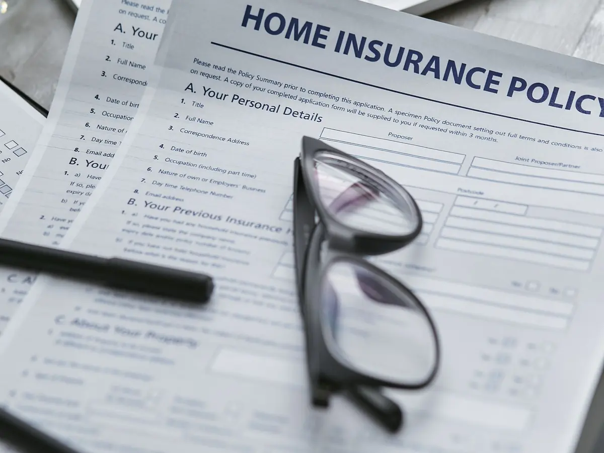 A home insurance policy form on a table with a pen and a pair of reading glasses resting on it