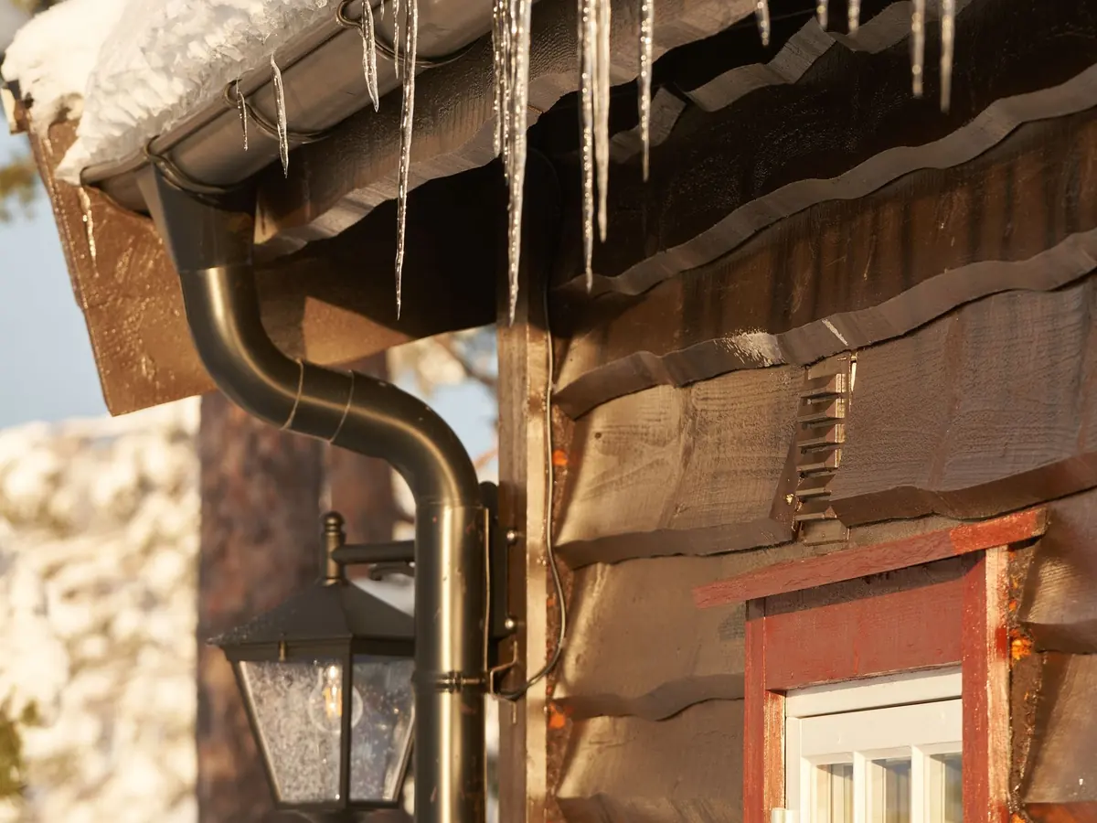 Long icicles hanging from the gutter along a porch roof, with a downspout and a lantern below