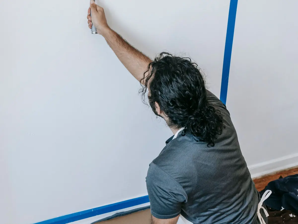 Painter rolling a fresh coat onto an interior wall with blue painter's tape masking the edge
